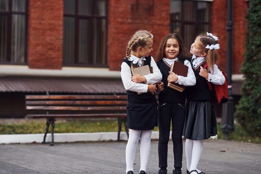 Groupe d'enfants de sexe féminin en uniforme scolaire qui est à l'extérieur ensemble près du bâtiment de l'éducation