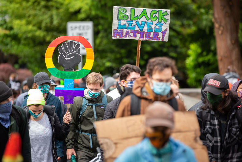 Un manifestant avec un masque facial BLM arc-en-ciel lève le poing en solidarité pendant la 