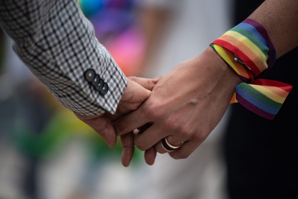 Un gros plan d'un couple de même sexe se tenant la main, l'un a un ruban arc-en-ciel enroulé autour de son poignet
