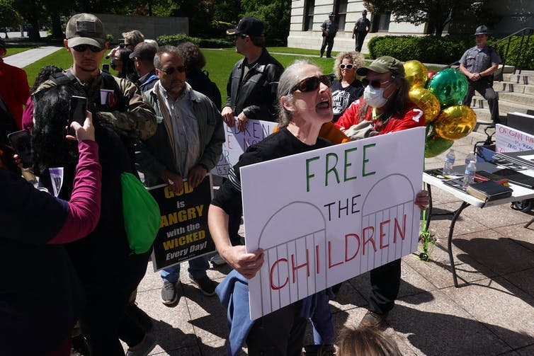 Une petite foule se tient sur une pelouse, certains tenant des pancartes comme « Free the Children »
