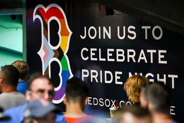 Les fans passent devant un logo des Red Sox de Boston avec un drapeau Progress Pride superposé dessus.