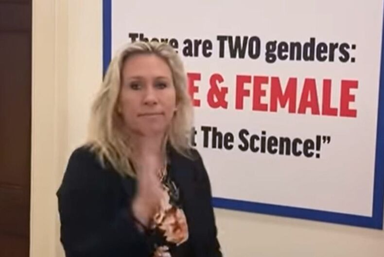 La représentante Marjorie Taylor Greene sourit à côté de son signe transphobe.