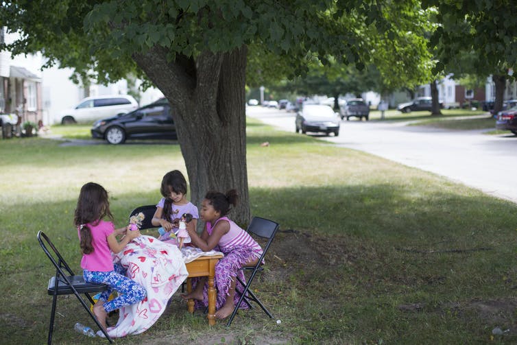 Trois jeunes filles jouent avec des poupées ensemble à une table à l'extérieur.