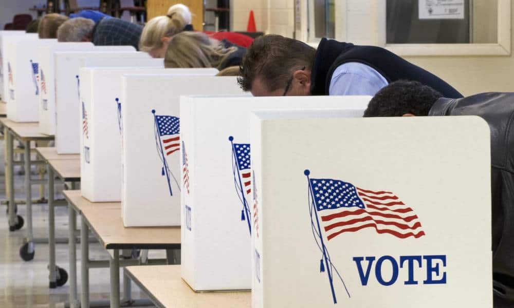 Plusieurs personnes sont penchées pour voter.  Leurs votes sont bloqués des téléspectateurs par un séparateur blanc avec un drapeau américain et le mot "voter" dessus