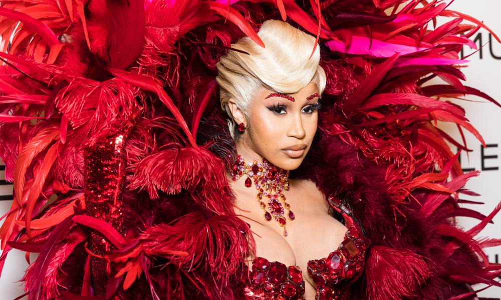 Cardi B porte un corsage rouge et a un énorme accessoire à plumes rouges derrière elle