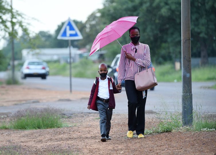Parent et enfant marchant ensemble main dans la main sous un parapluie.