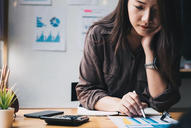 Une femme est assise à un bureau avec des papiers et une calculatrice.