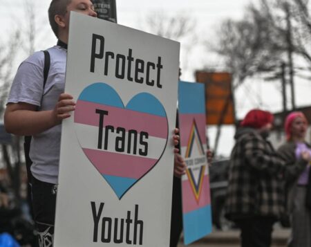 An activist holds a placard with the words 'Protect Trans Youth'