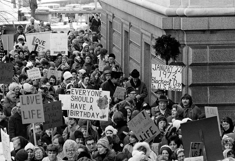 Une foule d'hommes et de femmes manifestant près d'un immeuble de la ville en hiver, brandissant des pancartes indiquant 