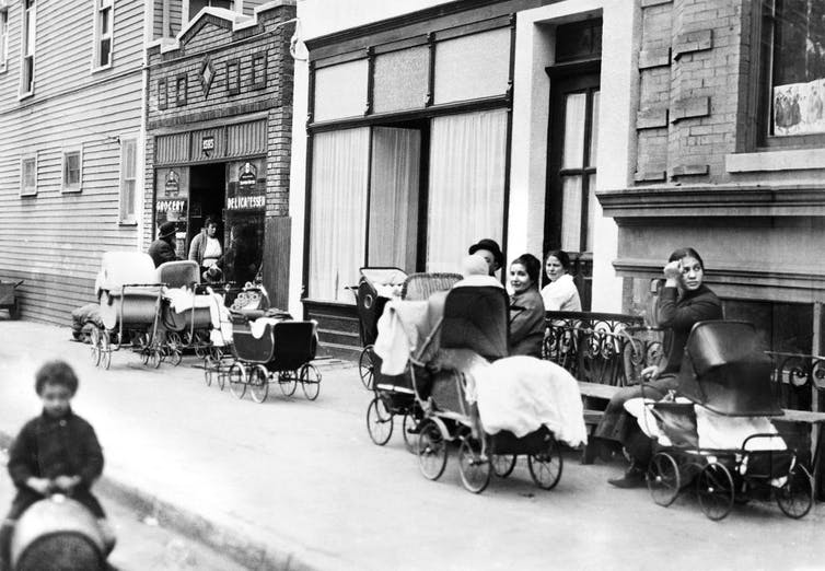 Une photographie en noir et blanc montre des femmes avec des poussettes alignées dans une rue.