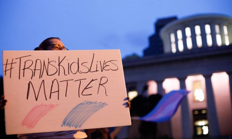 A transgender rights advocate holds a sign that reads '#TransKidsLives Matter' with pink and blue colours underneath as they outside the Ohio Statehouse during a rally against a trans sports ban bill