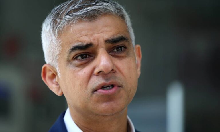 Sadiq Khan, the Mayor of London, wears a white collared shirt with a blue jacket as he stares slightly off camera