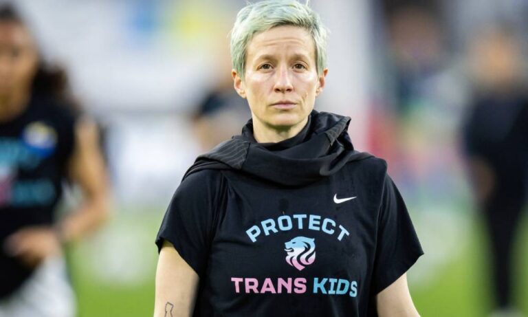 Megan Rapinoe dénonce les attaques « monstrueuses » contre les droits des trans aux États-Unis Megan Rapinoe stands on a soccer field while wearing a dark, short-sleeved t-shirt that has the words 'protect trans kids' written on it in blue and pink lettering