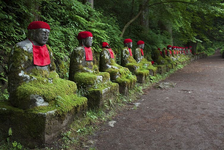 Une rangée de petites statues moussues de personnages assis le long d'un chemin dans la forêt.