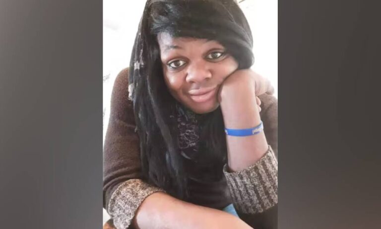 Brazil Johnson, a Black trans woman, wears a brown shirt and blue band on her write as she poses for a picture