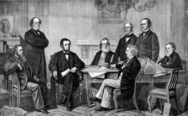 Sept hommes blancs se rassemblent autour d'une table pour regarder le président Abraham Lincoln signer la proclamation d'émancipation.