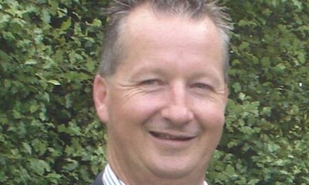 A headshot of Peter Keeley smiling in front of a bush