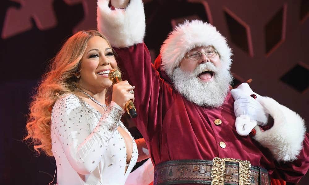 Mariah Carey chante dans un micro doré tout en portant une chemise blanche avec des strass dessus.  Elle est accompagnée sur scène par une personne déguisée en Père Noël en costume rouge et blanc avec une grosse ceinture marron et un chapeau rouge et blanc assorti
