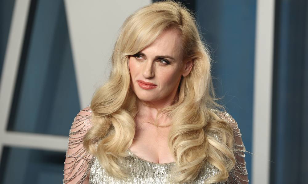 Rebel Wilson porte une robe argentée avec ses cheveux blonds baissés alors qu'elle pose pour la caméra