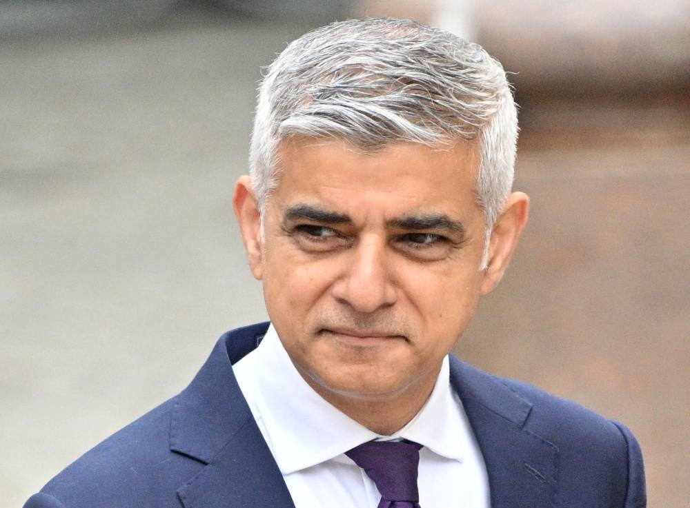 Sadiq Khan se tient à l'extérieur tout en portant une chemise boutonnée blanche, une cravate et une veste de costume bleue