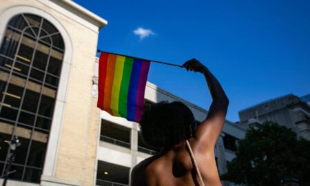 A person waves a rainbow LGBTQ+ Pride flag above their head