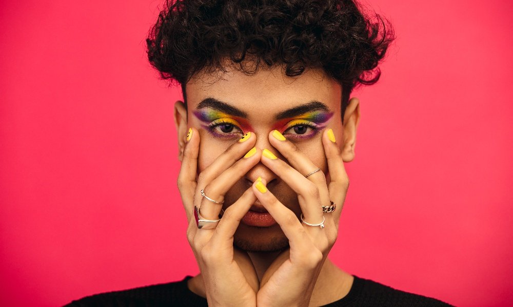 Personne fluide de genre portant un fard à paupières de couleur arc-en-ciel et un visage souriant sur l'ongle. 