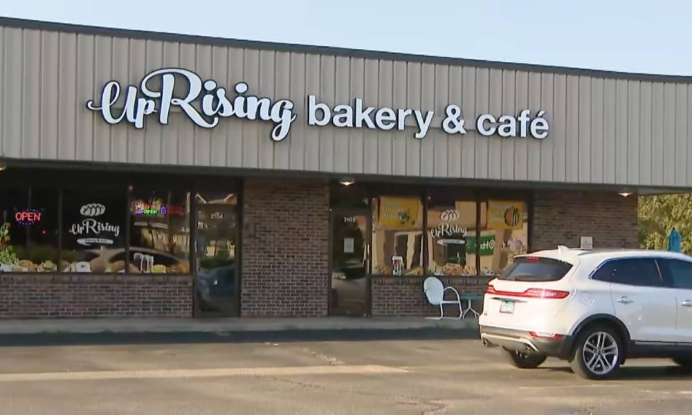 La boulangerie refuse de reculer après avoir reçu des menaces concernant des performances de traînée favorables à la famille The image shows a business front with the words 'UpRising Bakery and Cafe' written in white. A white car is parked outside in the parking lot