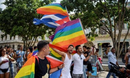 A crowd of people gather in the Prado avenue in Havana, Cuba holding up LGBTQ+ rainbow pride flags as well as the flag of Cuba