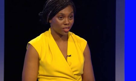 Kemi Badenoch wears a bright yellow outfit as she speaks at a podium during a Tory leadership election debate