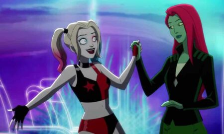 A still taken from the Harley Quinn animated series on HBO Max. In this image, Harley Quinn wears a black and red patterned outfit as she holds the hand of Poison Ivy, who is wearing dark clothing and staring at Harley