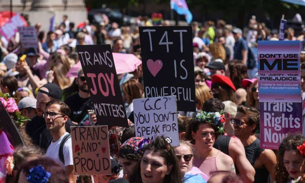 Plusieurs personnes se rassemblent pour soutenir la communauté trans au Royaume-Uni.  Une personne tient une pancarte indiquant «la joie trans compte» et une autre dit «trans et fier»