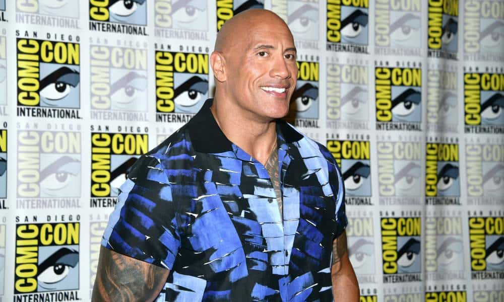 Dwayne « The Rock » Johnson a eu la meilleure réponse lorsqu’on lui a dit que jouer gay « ruinerait sa carrière » Dwayne 'The Rock' Johnson smiles for the camera as he wears a blue and black patterned top and stands in front of a patterned background with the SD Comic Con logo on it