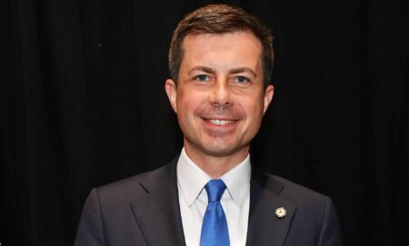 Pete Buttigieg smiles at the camera while wearing a suit and tie