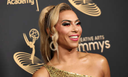 Shangela wears a gold dress as she stares somewhere off camera