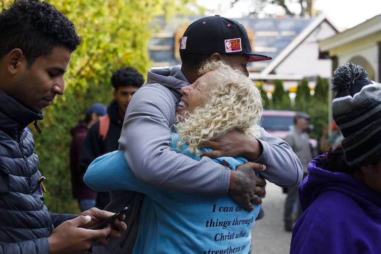 Une femme blonde aux cheveux bouclés embrasse un jeune homme latino portant une casquette de baseball.