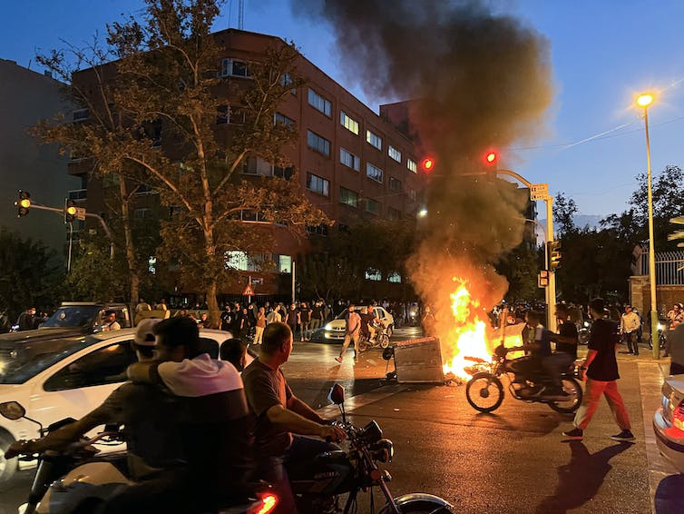 Un incendie flambe au milieu d'une rue en Iran alors que des centaines de personnes se rassemblent.