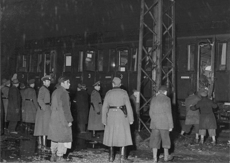 Des soldats regardent un train rempli de monde alors qu'une personne y est poussée.