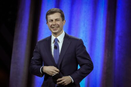 Pete Buttigieg speaks in front of a blue curtain