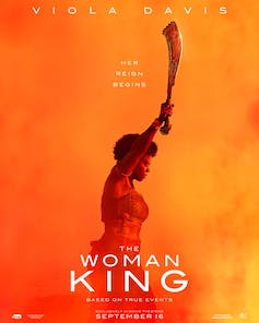Une affiche de film avec les mots The Woman King et une femme de profil levant une épée sur fond orange et jaune.