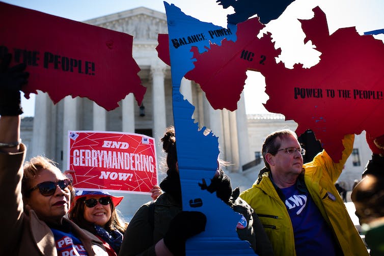 Les gens brandissent des cartes bleues et rouges découpées des États qui disent des choses comme «équilibrer le pouvoir» et un panneau indiquant «mettre fin au gerrymandering maintenant», devant la Cour suprême.