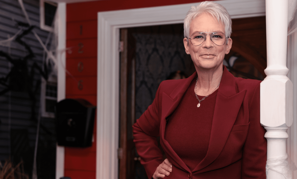 Jamie Lee Curtis porte une tenue rouge alors qu'elle s'appuie contre la balustrade d'une maison