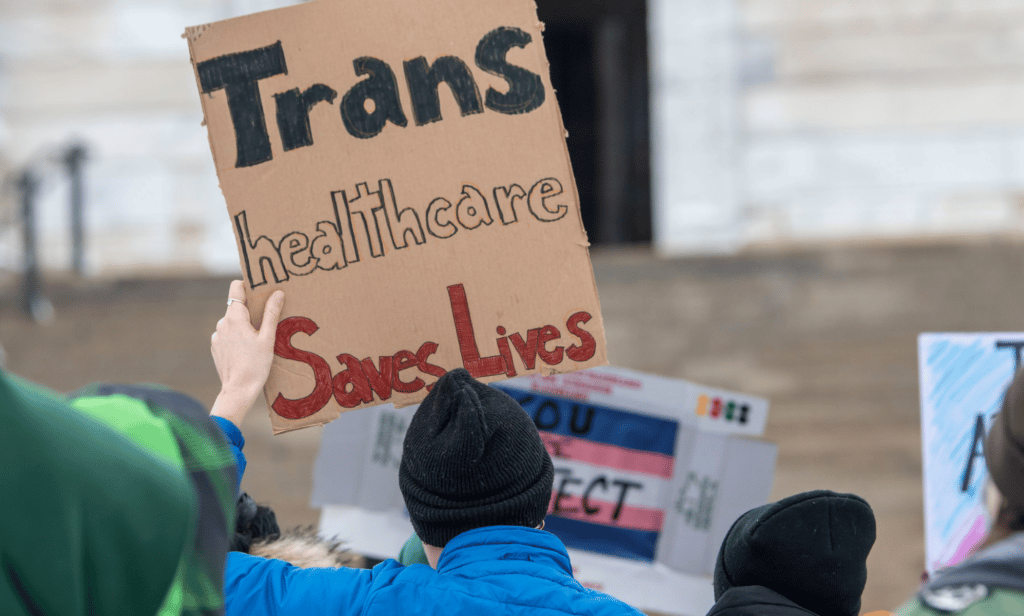 Les adolescents trans pourraient faire face à une détransition forcée et leurs parents emprisonnés en vertu de l’horrible projet de loi du Michigan A person holds up a sign reading 'trans healthcare saves lives'