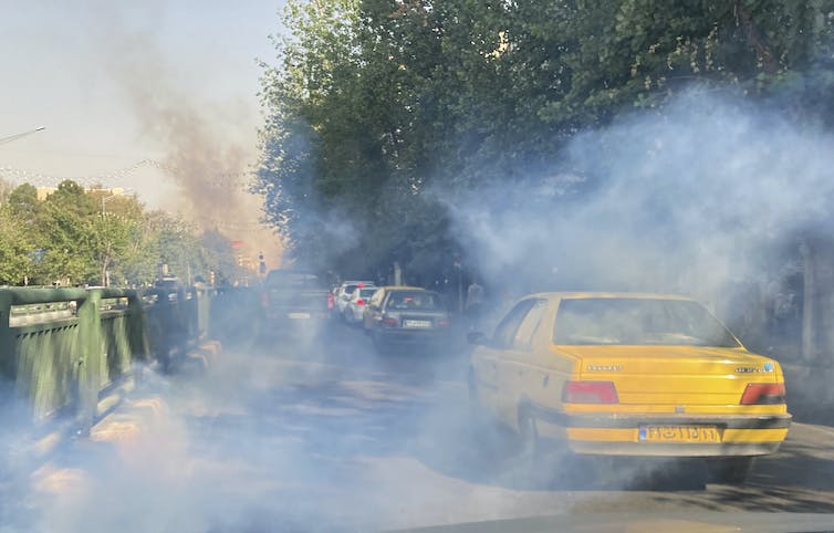 Une voiture jaune est vue au milieu d'un nuage de gaz lacrymogène.