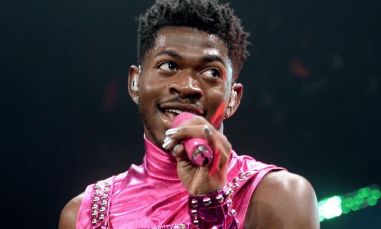 Lil Nas X wears a pink outfit as he sings into a microphone during a performance