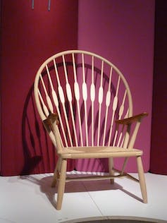 L'élégante chaise paon photographiée sur un riche fond magenta.  La chaise paon a un dossier large et rond qui imite le plumage d'un paon
