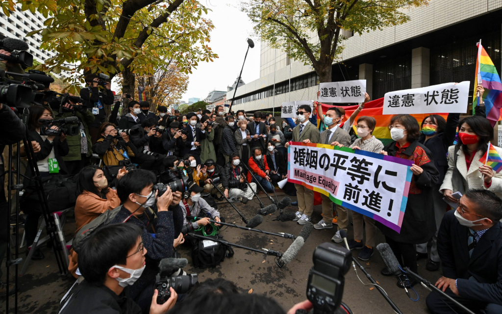 Une vue plus large de photographes entourant un groupe pro-LGBTQ+ agitant des banderoles en faveur du mariage homosexuel près d'un tribunal de Tokyo.