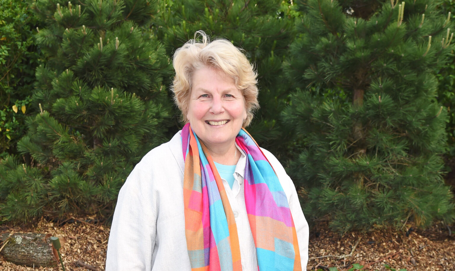La comédienne Sandi Toksvig annule les dates de sa tournée après avoir été hospitalisée pour une broncho-pneumonie Sandi Toksvig smiles for a photo wearing a rainbow scarf, with greenery in the background