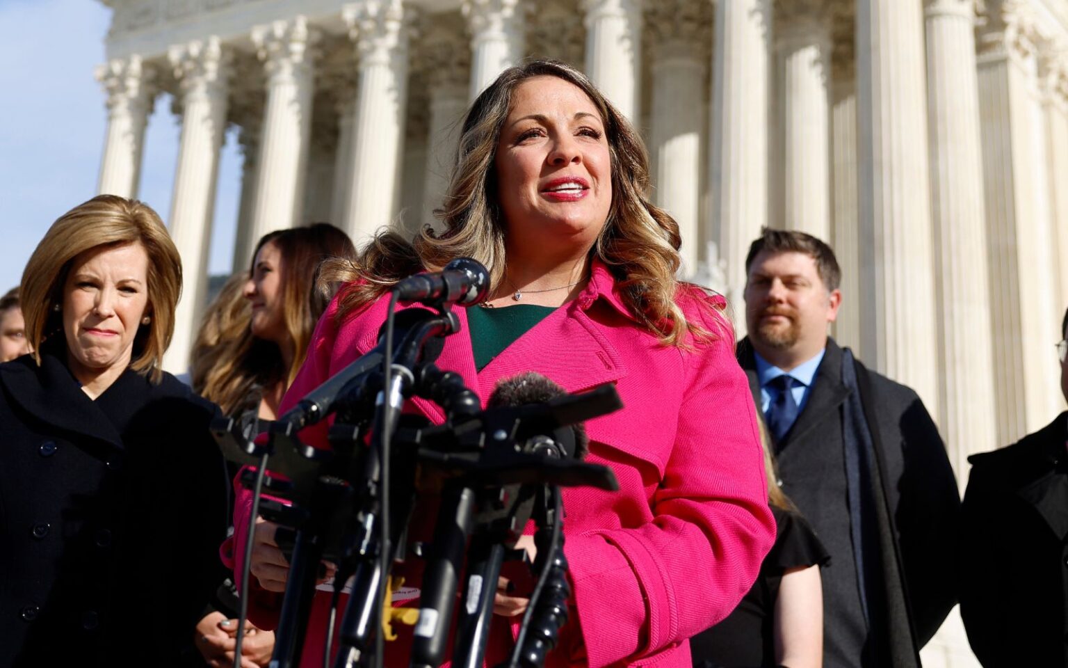 La Cour suprême décidera si une femme chrétienne peut refuser de travailler pour des couples de même sexe Lorie Smith, in a pink jacket, speaks outside the Supreme Court, with an array of microphones in front of her.