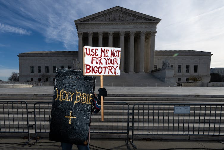 Une personne est bloquée par une grande fausse bible noire et tient une pancarte indiquant 