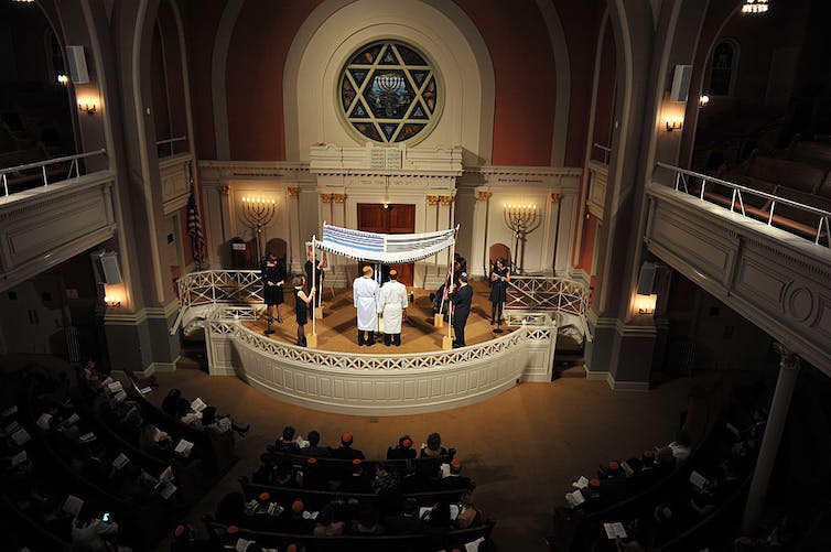Une synagogue sombre avec deux hommes se mariant à l'avant de la pièce.